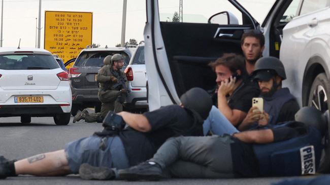 Journalists take cover behind cars as Israeli soldiers take position during clashes with Palestinian fighters near the Gevim Kibbutz, close to the border with Gaza on October 7, 2023. Picture: AFP