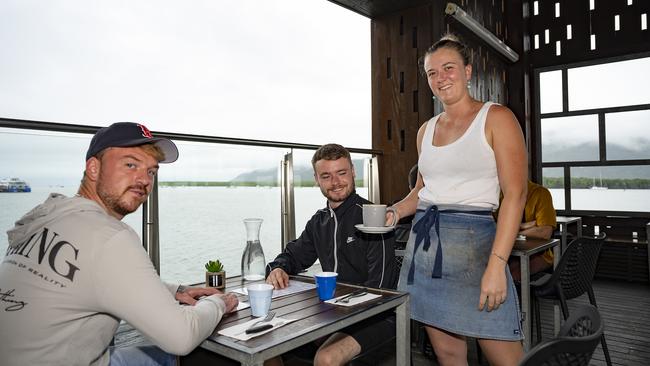 Wharf One Cafe manager Grace O’Connell serves British tourists Ben Goad and Billy Quick a coffee during a chilly Cairns morning on Tuesday. Picture Emily Barker.