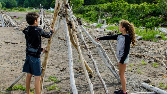 Boy and girl making a teepee with tree trunk found on the beach of the St. Lawrence river in Gaspesie (Les Mechins) during summer day vacations.