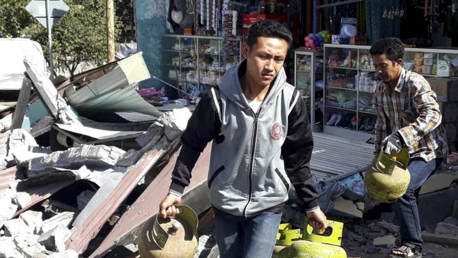 Residents carry gas tanks they recovered from a building damaged by the earthquake on Lombok Island. Picture: AP