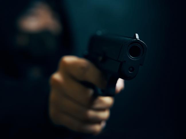 Man in hood threatens with firearm. Masked robber with gun. Weapon in person's hands. Murderer or armed thief. Criminal with pistol. Generic image. Picture: Savusia Konstantin