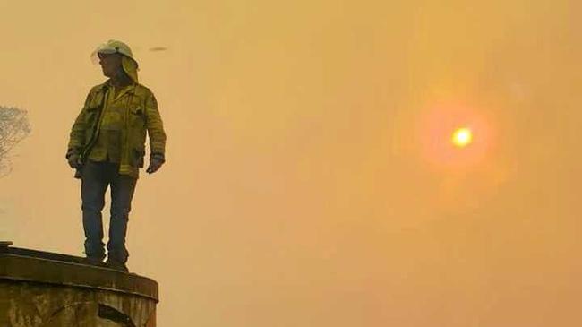 Ewingar burns as RFS assess the situation from a water tank. Picture: Nadine Gaffney