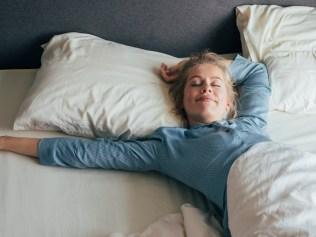 Smiling young woman stretching her arms in bed on a sunny morning.