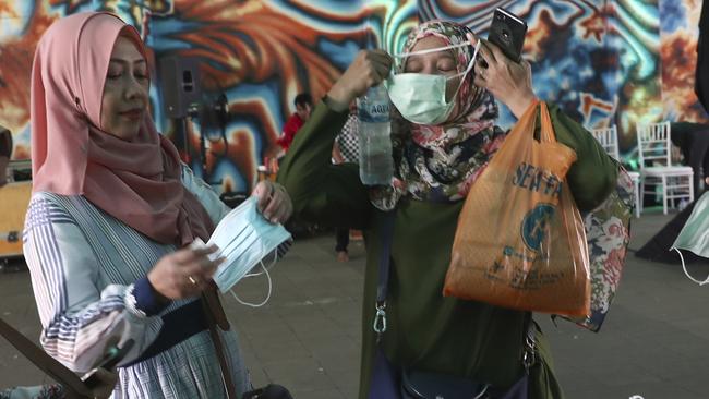 Women prepare to put on masks near a Mass Rapid Transit station in Jakarta, Indonesia. Picture: AP