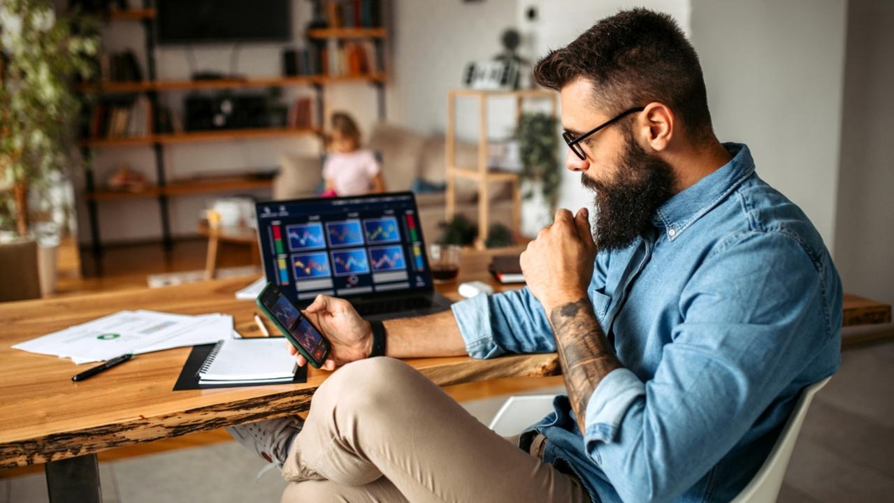 Mid adult handsome man working at home using laptop, while his daughter doing her homework in background in living room