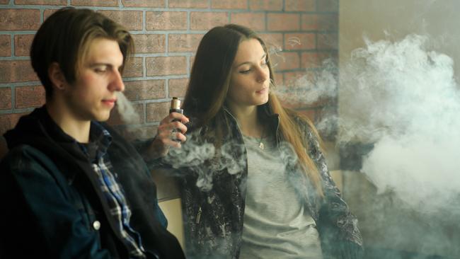 Vape teenagers. Young cute girl in sunglasses and young handsome guy smoke an electronic cigarettes in the vape bar. Bad habit that is harmful to health.