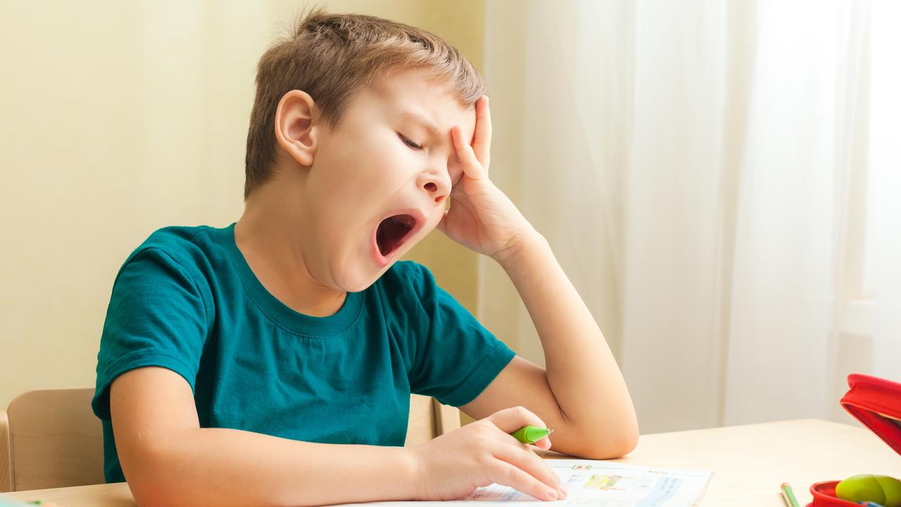 A young boy yawns while sitting at a desk doing schoolwork. Picture: iStock