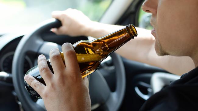 The concept of alcohol driving crime - closeup of young male driver hands with steering wheel and bottle of beer. Drink driving generic. Picture: iSTOCK