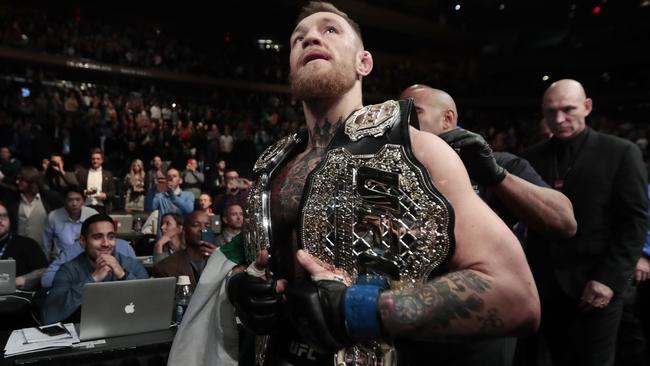 Conor McGregor leaves the octagon with his title belts after knocking out Eddie Alvarez.