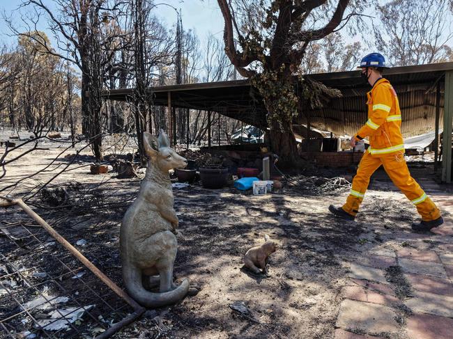 A man in a fire suit walks past an ornamental statue of a kangaroo in the yard of a razed house after bushfires in Gidgegannup, some 40 kilometres north-east of Perth on February 4, 2021. (Photo by Trevor Collens / AFP)