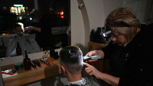 This Ukrainian hairdresser works by torchlight because a Russian attack took out the power. Chris Bowen does not have that good an excuse for causing blackouts here. Picture: AFP