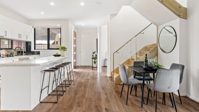 The kitchen features a stone-topped island breakfast bench, sleek mirror splashback, storage space and stainless-steel appliances