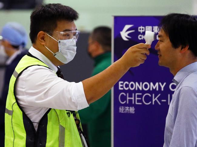 A worker checks a passenger’s temperature at Sydney International Airport. Picture: Matrix