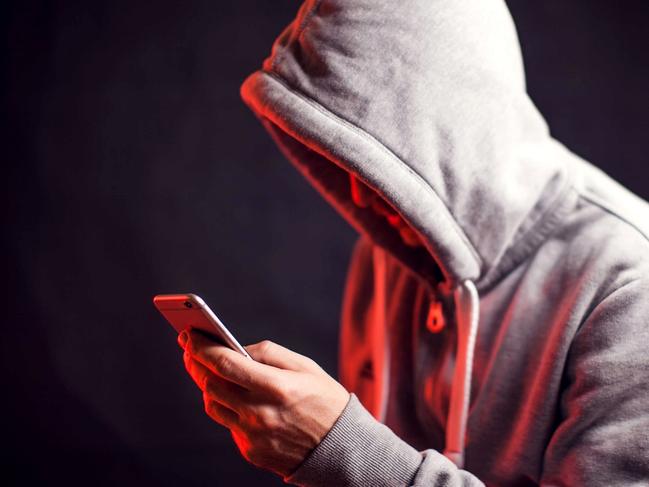 Man wearing hoody sweater with mobile phone in hands. Crime and hacking concept; scam generic.