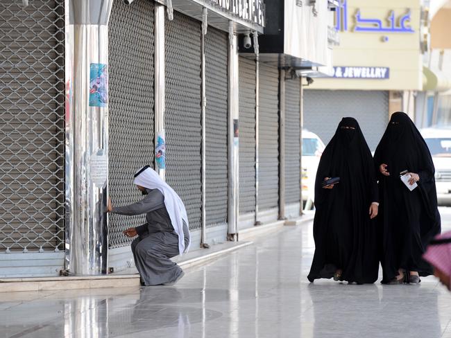 Saudi women walk past a jeweller arriving to open his shop in the Tiba gold market in the capital Riyadh on February 27, 2018. The Riyadh gold souk is short of salesmen after a government edict to replace foreign workers with Saudis as part of contentious efforts to tackle high unemployment, with many of them who have been long accustomed to a generous cradle-to-grave welfare system regard such jobs as degrading. / AFP PHOTO / Fayez Nureldine