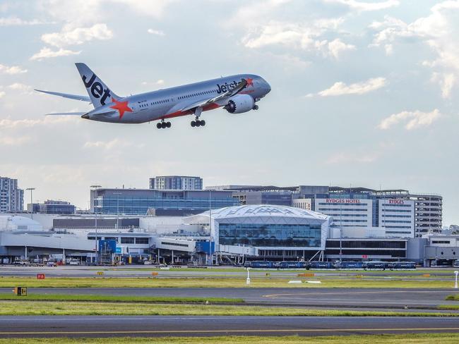 A Jetstar Airways B787-8 (VH-VKH) takes off towards the north on the main runway of Sydney Kingsford-Smith Airport and is heading to Honolulu.  A row of ground transport buses is parked near to the terminal.  In the distance is the international terminal, and beyond that, nearby hotels and residential towers.  This image was taken from Shep's Mound, a public viewing area off Ross Smith Avenue, at sunset on 18 February 2023.Escape 15 October 2023Doc Holliday - Airports ExtraPicture : iStock