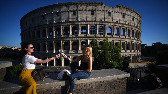 Young women clink bottles of beer as they share an drink by the Colosseum monument in Rome as the country eases its lockdown after more than two months. Picture: Filippo Monteforte/AFP