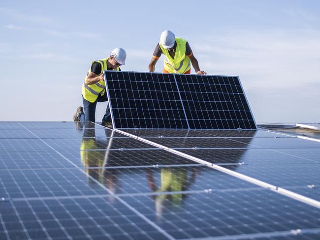 Team of two engineers installing solar panels on industrial factory roof.