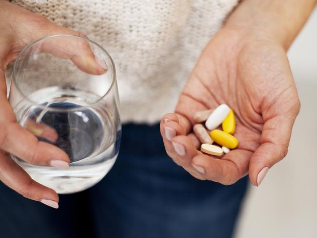 unrecognizable woman holding vitamins in one hand and water in the other