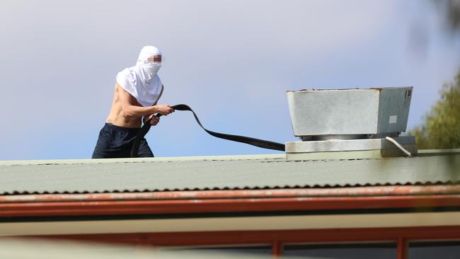 A youth with a fire hose on the roof of Parkville Juvenile Justice Centre. Picture: Alex Coppel