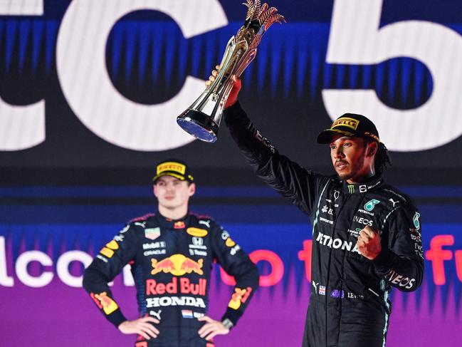 TOPSHOT - Winner Mercedes' British driver Lewis Hamilton (R) reacts with his trophy flanked by second-placed Red Bull's Dutch driver Max Verstappen (L) during the podium ceremony after the Formula One Saudi Arabian Grand Prix at the Jeddah Corniche Circuit in Jeddah on December 5, 2021. (Photo by ANDREJ ISAKOVIC / POOL / AFP)