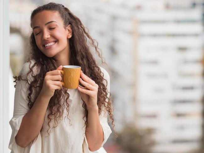 Happy business woman enjoying her hot beverage at work