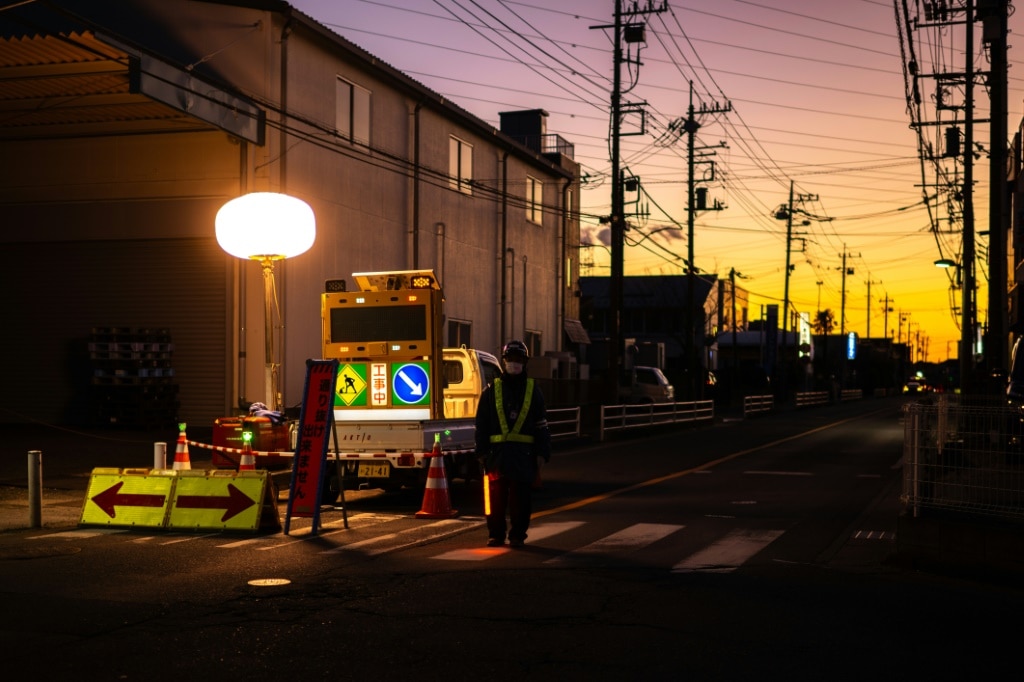 A worker controls the traffic as rescue operations continue for a truck driver after his vehicle plunged into a sinkhole in Yashio