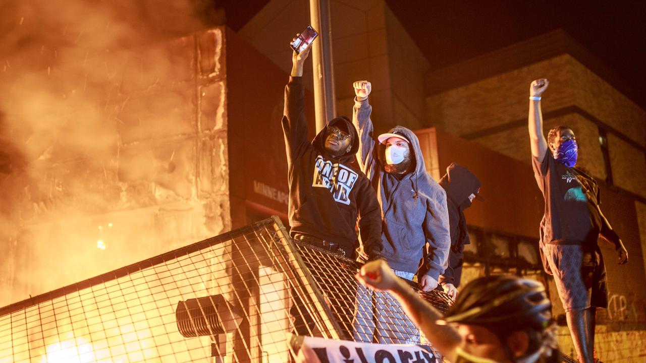 Protesters hold up their fists as flames rise behind them in front of the 3rd Precinct after it went up in flames. Picture: AFP