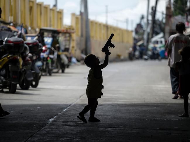 A child is silhouetted while playing with a toy gun as police officers conduct a house-to-house campaign on illegal drugs at a Manila slum on October 6, 2016. Picture: Noel Celis