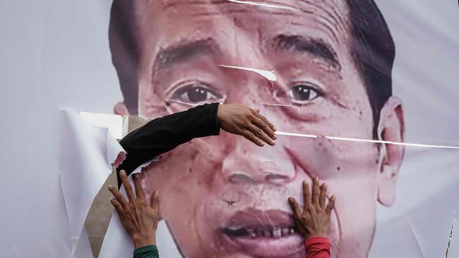 Counter-protesters fix a ripped banner portrait of Joko Widodo as they rally in Jakarta against a demonstration demanding his impeachment. Picture: AFP