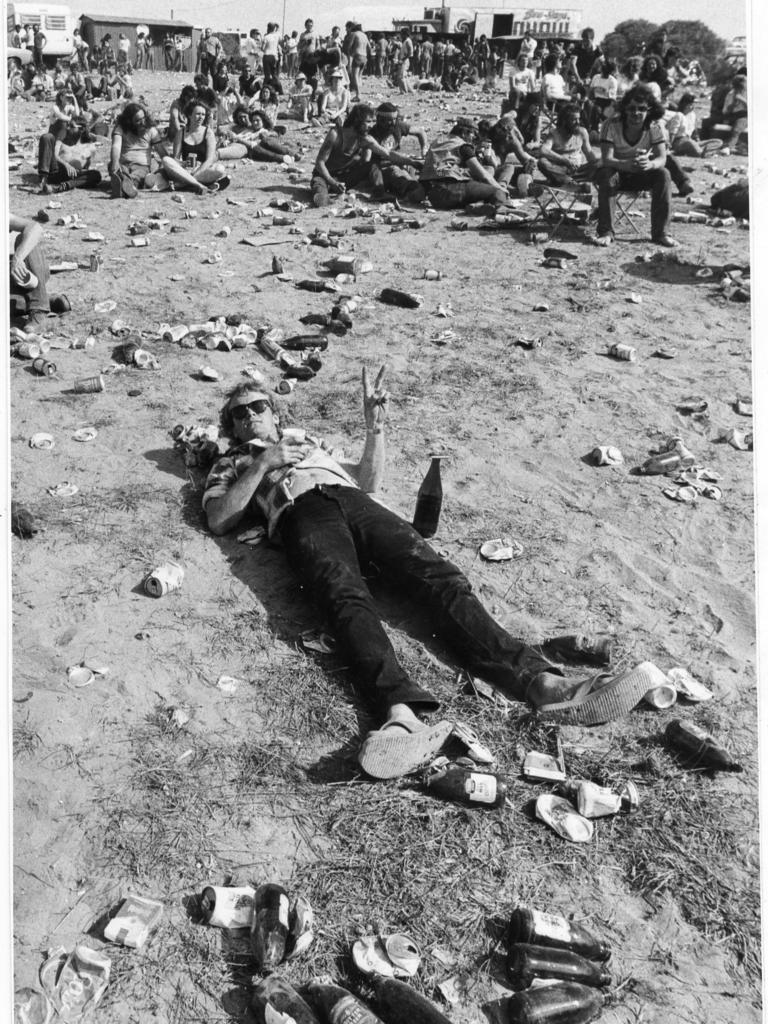 A music fan laying down among the litter of cans and bottles at Ponde rock music festival, held by the Hell's Angels Motorcycle Club in Ponde near Mannum, SA, 19 Oct 1983.