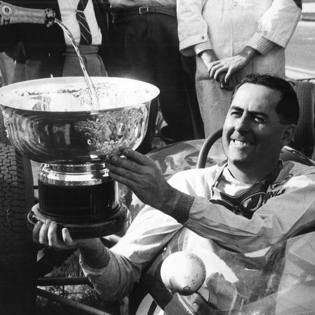 Jack Brabham celebrates his first place with a trophy of champagne at the 1964 Grand Prix. Picture: News Corp Australia