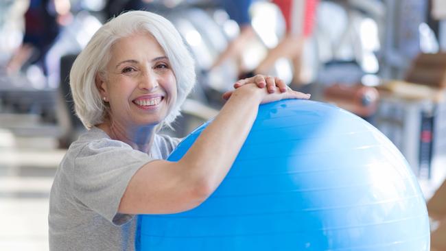 Finishing training. Pleasant beautiful senior woman smiling and keeping fit ball while sitting on a floor in a gym. Healthy baby boomers and seniors, generic retirement