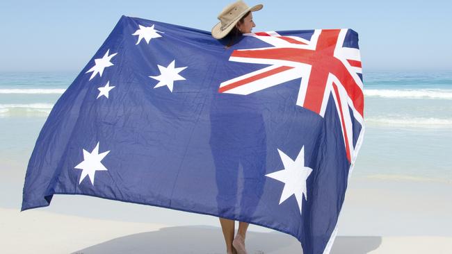 Attractive mature woman wearing akubra hat and with Australian flag around shoulder standing at tropical Australian beach, isolated with ocean and blue sky as background and copy space.