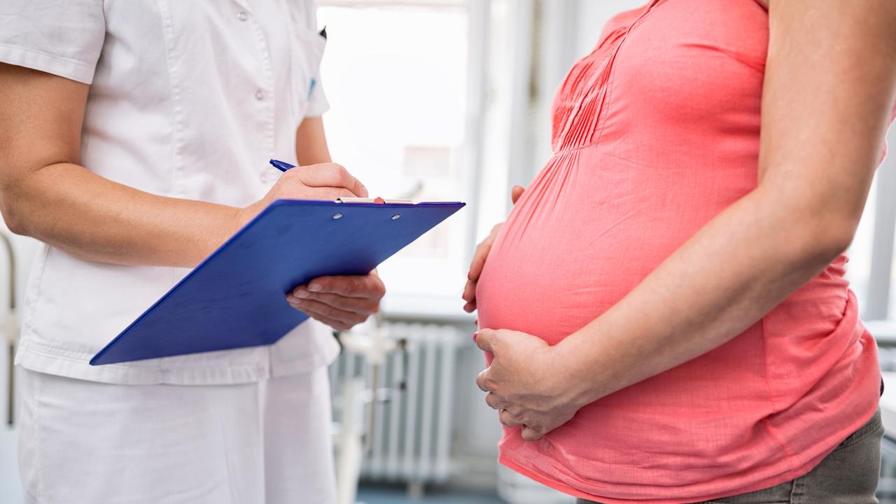 Nurse checking weight of pregnant woman in hospital room.