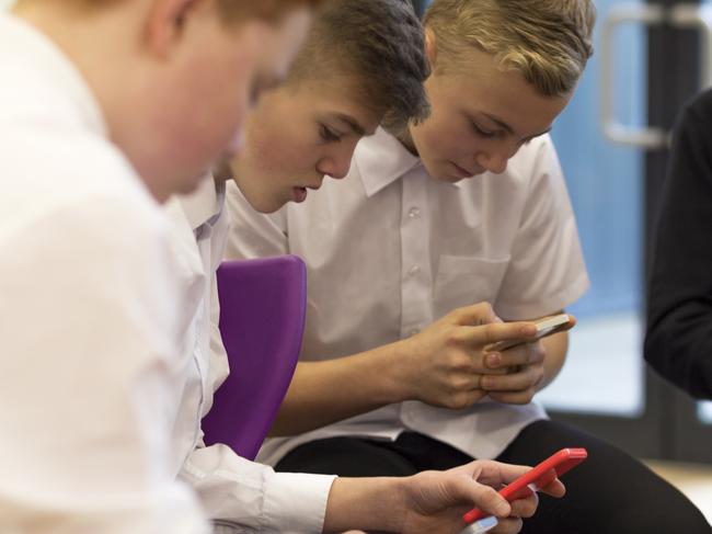 Group of male high school students on their break at school. They are all looking at smartphones.