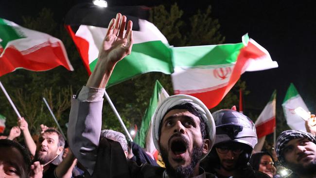 TOPSHOT - Demonstrators wave Iran's flag and Palestinian flags as they gather in front of the British Embassy in Tehran on April 14, 2024, after Iran launched a drone and missile attack on Israel. Iran's Revolutionary Guards confirmed early April 14, 2024 that a drone and missile attack was under way against Israel in retaliation for a deadly April 1 drone strike on its Damascus consulate. (Photo by ATTA KENARE / AFP)