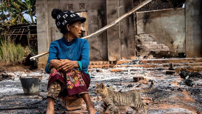 A woman sits next to a cat in front of her damaged house following fighting between Myanmar's Military and the Kachin Independence Army in Nam Hpat Kar, Kutkai township.