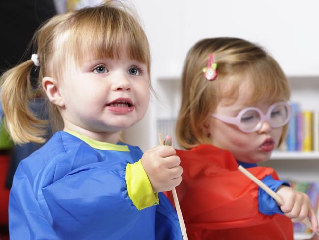 A portrait of a group of  toddlers painting whilt their carer tidies.