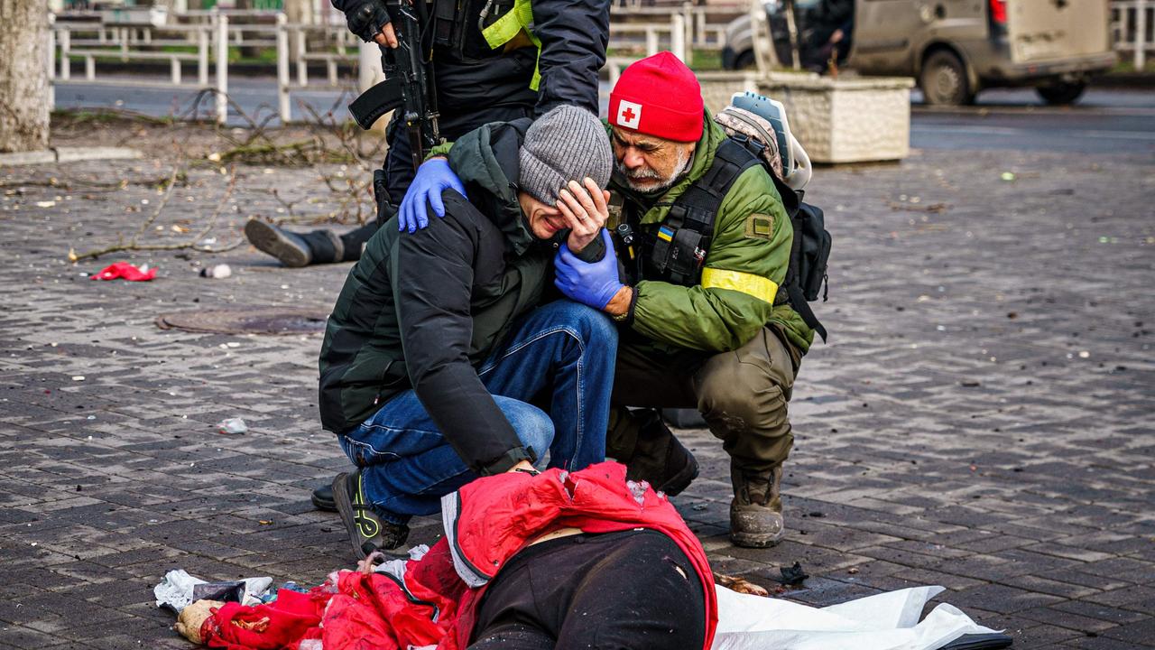 A rescuer and Ukrainian police officer comfort a man as he reacts next a body of a dead woman after Russian shelling to Ukrainian city of Kherson on December 24, 2022. (Photo by Dimitar DILKOFF / AFP)