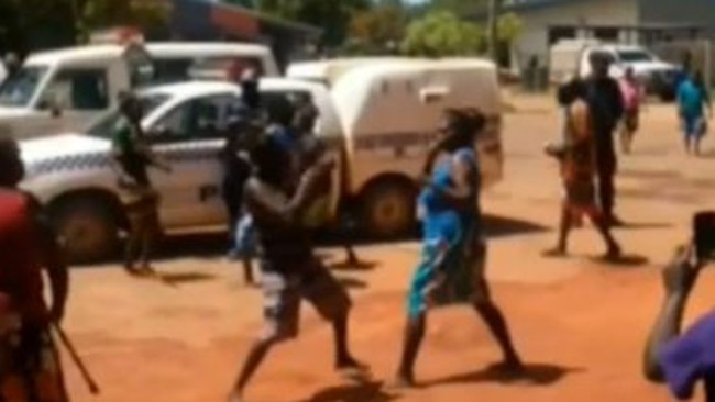 Police watch in the background as two women throw punches at each other in the Queensland community of Aurukun.