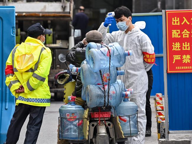 A man wearing a protective suit takes the temperature of a worker in Wuhan. Picture: AFP