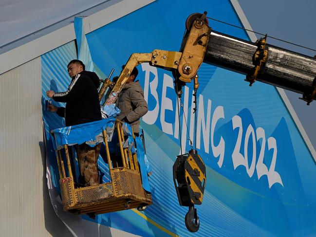 Workers set up a banner on the sign of a building at the Beijing Olympic Park. Picture: Noel Celis / AFP