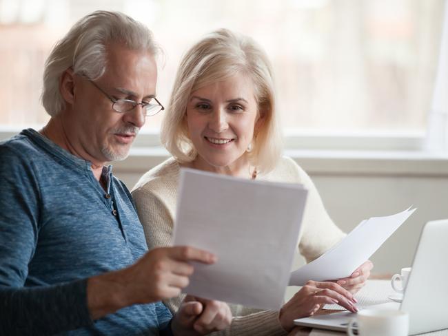 Happy old middle aged couple holding reading good news in document, smiling senior mature family excited by mail letter, checking paying domestic bills online on laptop, discussing budget planning