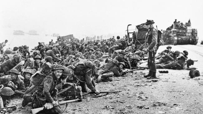 British soldiers crouching on the beach immediately after the D-Day landing, waiting for a tank to pass by before they advance inland in Normandy, France, 1944. Picture: AAP / Australian War Memorial