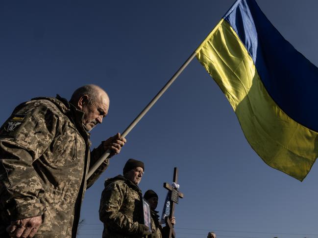 FASTIV, UKRAINE - FEBRUARY 24: A soldier holds a flag during the joint military funerals for Volodymyr Semenyuk, 43, and his military comrade Serhiy Voytenko, 53, on February 24, 2025 in Fastiv, Ukraine. Both soldiers were with the 47th brigade, killed together on February 18th in Kursk (Russia) when a glide bomb hit their position. Monday marks three years since Russia launched a full-scale invasion of Ukraine, with Russian forces continuing to make slow but steady gains across Ukraine's eastern front, while Ukrainian forces have staged a counter-offensive into Russian territory. The milestone comes as tensions between Ukraine and its key ally, the United States, have been escalating since  Ukraine was excluded last week from bilateral talks between American and Russian diplomats, on laying the groundwork for peace negotiations. (Photo by Paula Bronstein/Getty Images)