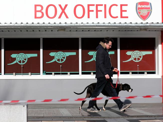 A pedestrian walks his dog outside the Emirates Stadium in London in London on March 13, 2020. - The English Premier League suspended all fixtures until April 4 on Friday after Arsenal manager Mikel Arteta and Chelsea winger Callum Hudson-Odoi tested positive for coronavirus. (Photo by ISABEL INFANTES / AFP)