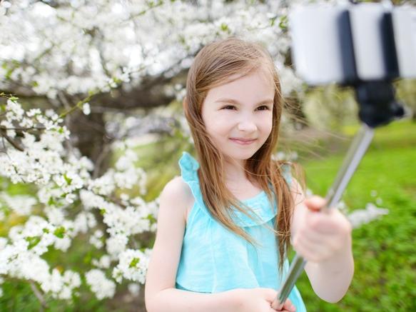 Adorable little girl taking a photo of herself with a selfie stick on beautiful summer day