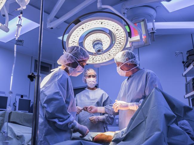 Doctors wearing surgical masks and gowns performing an operation on patient in hospital operating theater.