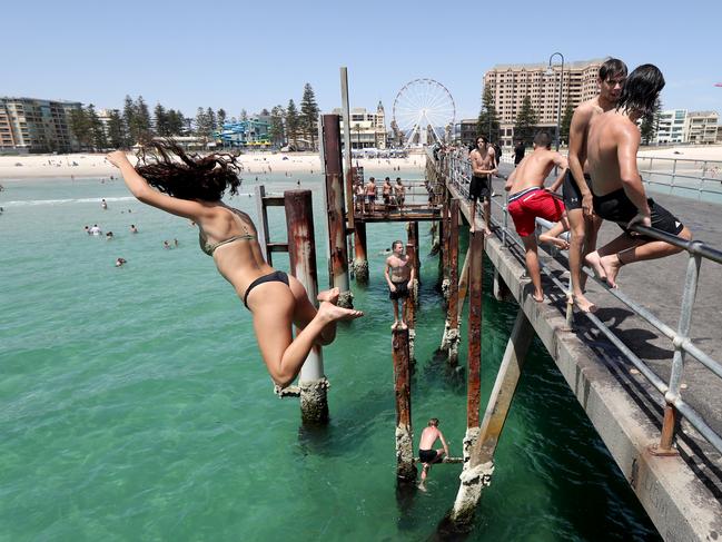 Teens jump of the jetty at Glenelg beach during a hot day in Adelaide, Tuesday, January 22, 2019. (AAP Image/Kelly Barnes) NO ARCHIVING